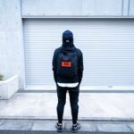 man in black hoodie and blue denim jeans standing on gray concrete floor